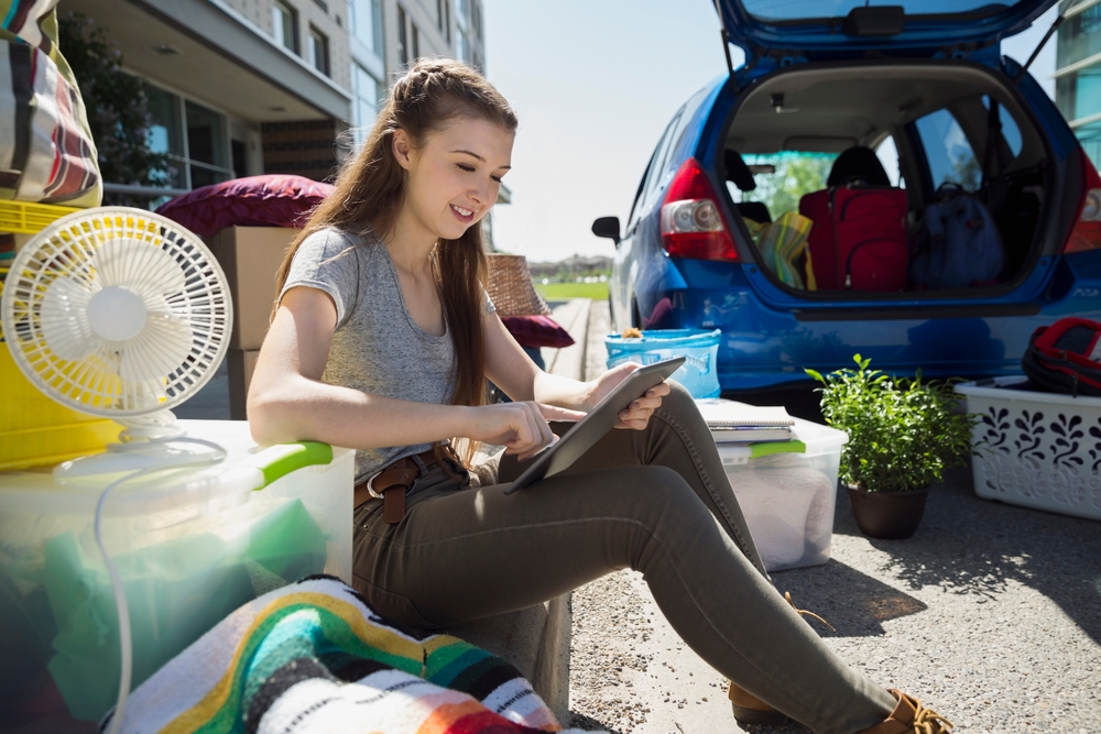 College student on tablet, moving belongings into car