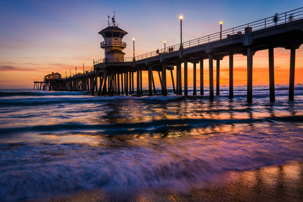 Waves crashing on the shore with a pier in the background during sunset