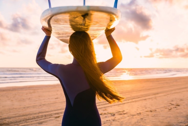 woman holding surfboard on beach with sunset