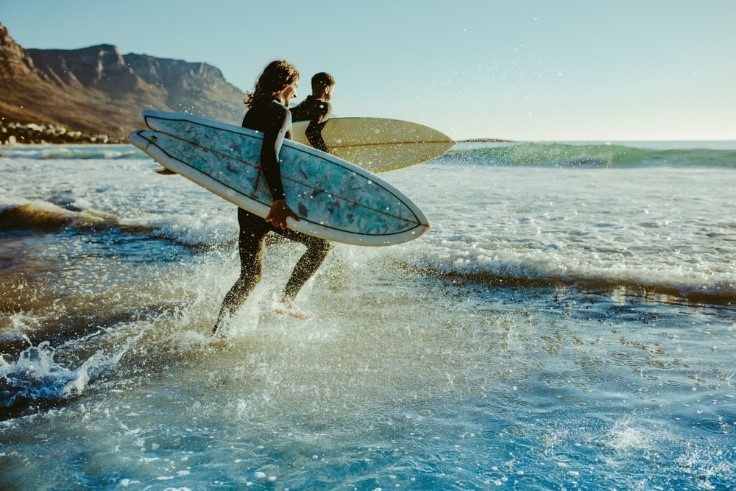 people running in ocean with surfboards